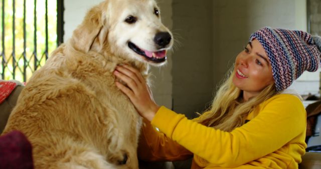 Happy caucasian female teenager wearing cap petting her dog at home. Domestic life, pets, animals and care, unaltered.