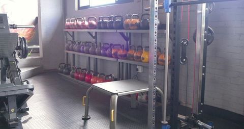 Displaying colorful kettlebells on industrial metal rack beside bench and power rack