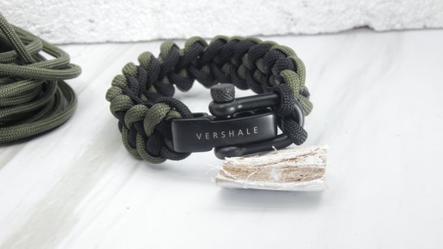 Close-up shot of a paracord survival bracelet featuring black and green woven cords, Vershale branding on the clasp, and a flint stone. Ideal for showcasing outdoor gear, survival tools, and tactical accessories. Perfect for ecommerce listings, DIY survival gear blogs, and adventure preparation guides.