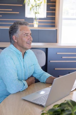 Mature man working on laptop in home office wearing blue shirt