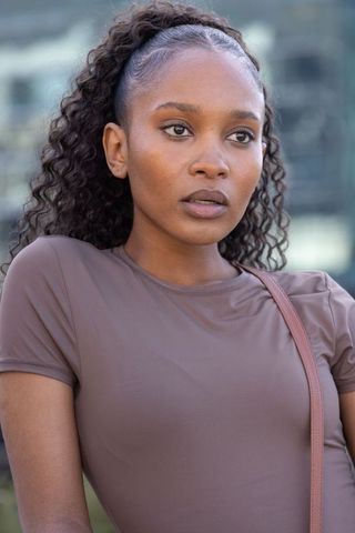 Confident young woman wearing fitted brown top by glass facade urban headshot
