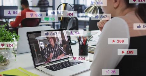 Woman Watching Virtual Meeting on Laptop with Social Media Metrics Overlay in Open Office