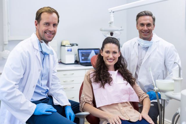 Dentists and female patient smiling in a dental clinic. Ideal for use in healthcare promotions, dental care advertisements, medical team presentations, and patient care brochures. Highlights professional dental services and patient satisfaction.