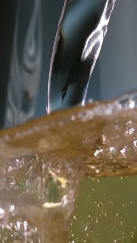 Vertical close-up video of faucet pouring water into glass forming frothy bubbles and splash