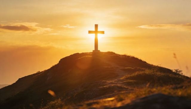 Sunrise cross silhouette on hilltop ridge with golden halo and pathway to summit