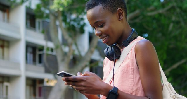 Young African American woman texts on her phone outdoors, with copy space. She enjoys a sunny day while staying connected with friends.