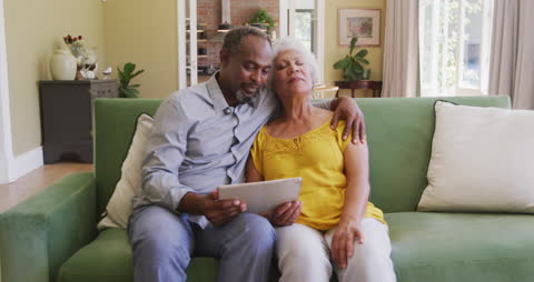 Senior Couple Embracing on Sofa Using Tablet in Home