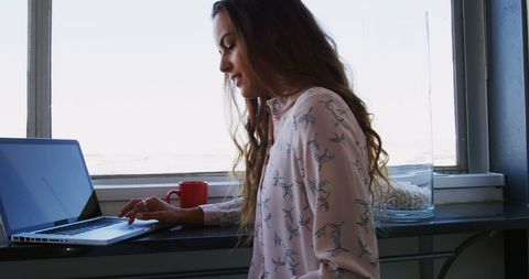 Young Woman Focused on Laptop Work Beside Window