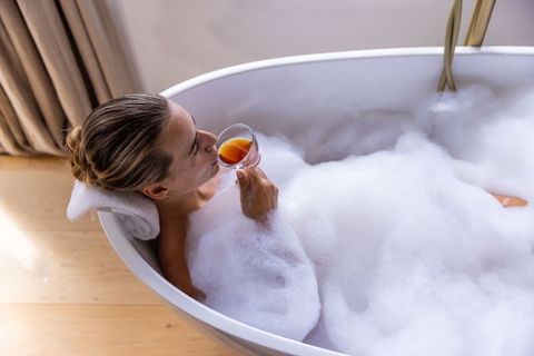 Woman soaking in foam bubble bath while sipping tea in luxury freestanding tub