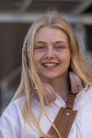 Young woman smiling with pink headphones at urban transit station, windswept hair