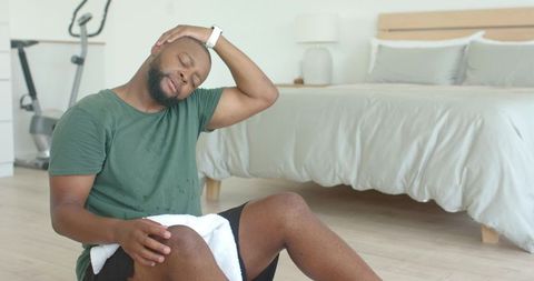 African american man stretching and cooling down after home workout in bright bedroom