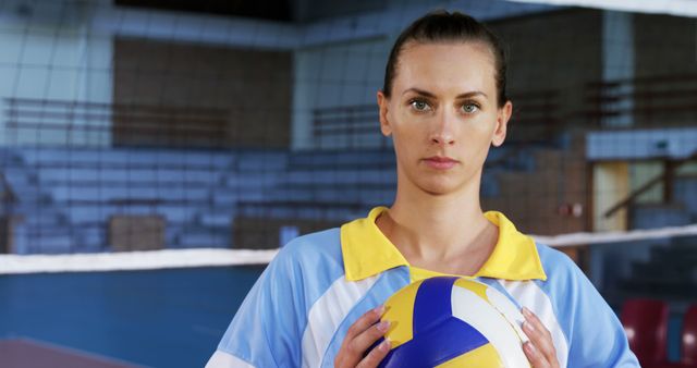 Female volleyball player holding ball standing on indoor court. Ideal for articles on sports, women's athletics, volleyball training, team dynamics, posters, and fitness promotions.