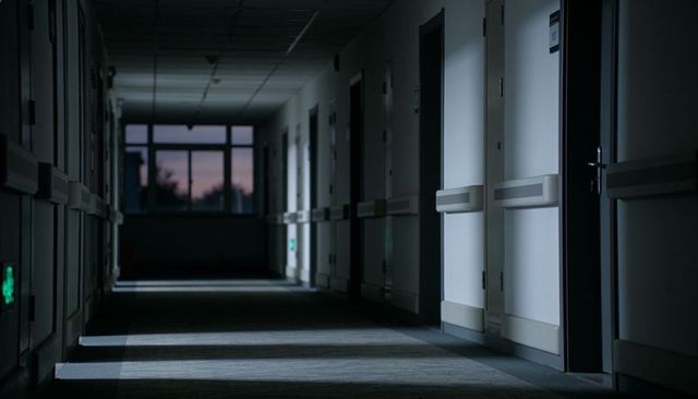 Empty hospital corridor leading toward dusky window on upper floor at twilight