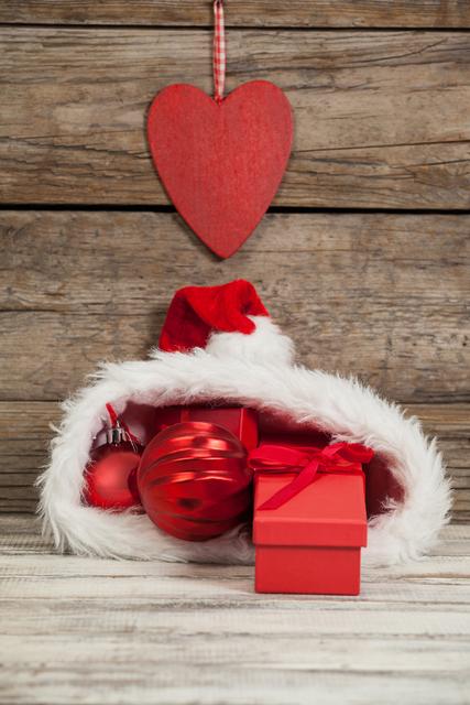 Perfect for holiday-themed advertisements, greeting cards, and festive social media posts. The image captures the essence of Christmas with red baubles and gifts inside a Santa hat, set against a rustic wooden background. Ideal for promoting Christmas sales, holiday events, and seasonal decorations.