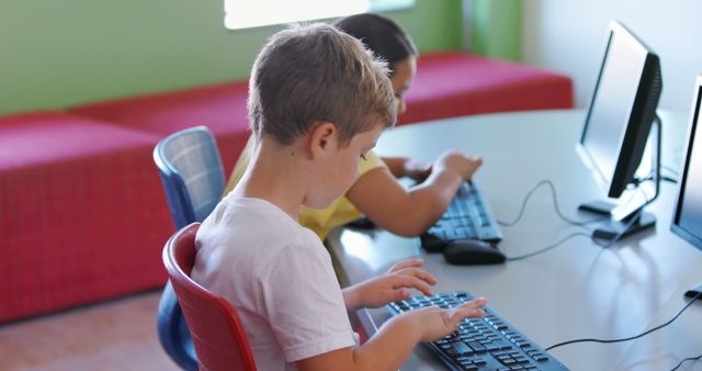 Children sitting at tables, practicing typing on computer keyboards. Useful for depicting educational environments, technology in education, digital literacy, and modern learning settings. Ideal for school promotional materials, educational articles, or technology-focused educational content.