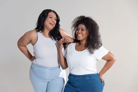 Two women laughing and bonding in casual white tops and denim, body positive portrait
