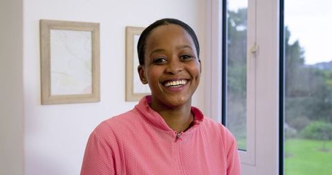Bright natural portrait of African American woman smiling in pink zip-up, cheerful daylight interior