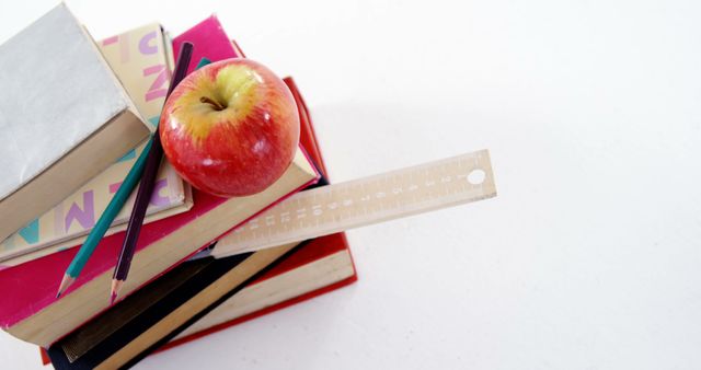 Stacked school books, a red apple, pencils, and a ruler are arranged on a white background, with copy space. These items symbolize education and the traditional concept of a teacher's resources.