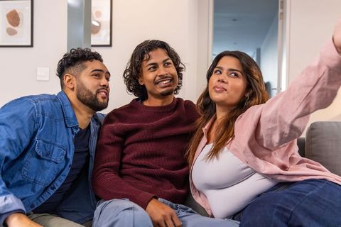 Indian friends taking selfie on living room couch during relaxed casual hangout in home