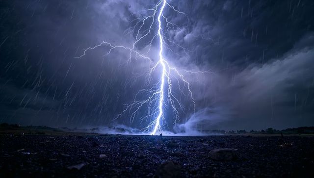 Powerful forked lightning striking wet gravel during nocturnal thunderstorm rain streaks