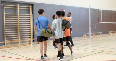 Multiracial male volleyball team walking into gym carrying duffel bags preparing for practice