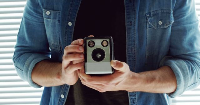 A Caucasian man in a denim shirt holds a vintage camera, with copy space. Capturing the essence of retro photography, his stance suggests a passion for classic imagery.