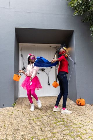 African american girls playing superheroes in halloween costumes holding pumpkin buckets