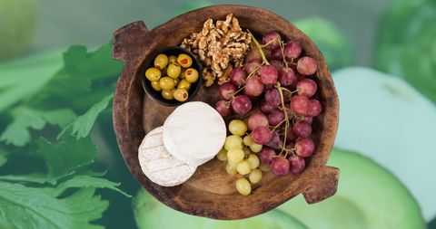 Wooden bowl of cheese, grapes and olives on greens