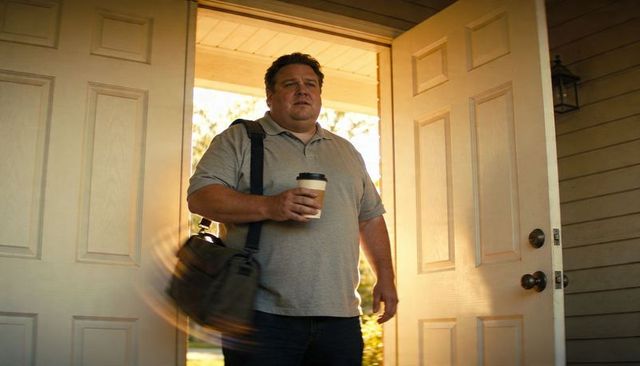 Middle-aged man entering sunlit front door holding coffee and messenger bag on commute