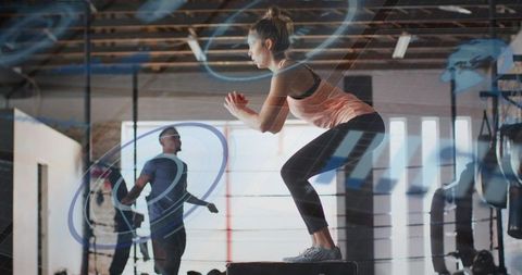 Female athlete performing plyometric box jump in industrial gym with rope skipping
