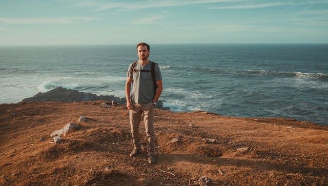 Standing male hiker on coastal cliff overlooking ocean at golden hour