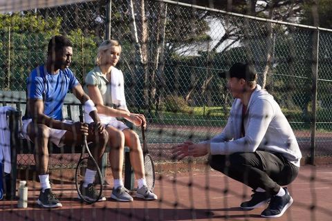 Coach briefing diverse tennis players on strategy during outdoor park training, teamwork