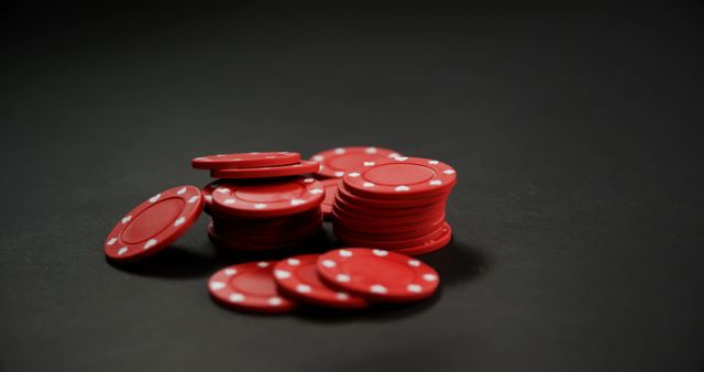 This image depicts a pile of red poker chips arranged on a dark background, which emphasizes the vibrant color of the chips. It is perfect for use in articles and advertisements related to gambling, casinos, poker games, betting strategies, and entertainment involving poker games. Suitable for promoting casinos, poker tournaments, gaming events, or online gambling platforms.