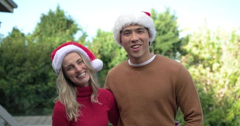 Smiling couple wearing santa hats on sunny backyard deck celebrating casual outdoor holiday moment