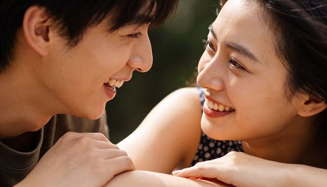 Sunlit young couple smiling and gazing at each other in park close-up