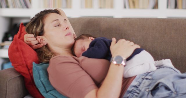 Mother lying on a sofa with her sleeping newborn baby on her chest, conveying themes of relaxation, bonding, and peacefulness. Ideal for use in blogs, articles, and marketing materials related to parenting, family life, motherhood, and home comfort.