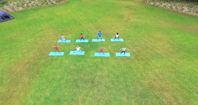 Group practicing yoga on grass field from an aerial perspective. Ideal for promoting fitness and wellness programs, outdoor activities, group workouts, and mindfulness. Could be used for fitness magazines, wellness blogs, online yoga courses, or advertisements for outdoor fitness events.