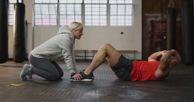 Caucasian muscular man exercising, doing sit ups with female coach. health and fitness training at gym.