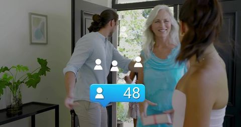 Senior woman entering home with wrapped gift while hosts greeting arriving guests