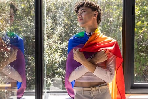 Pride and self-love: man draped in rainbow flag near window