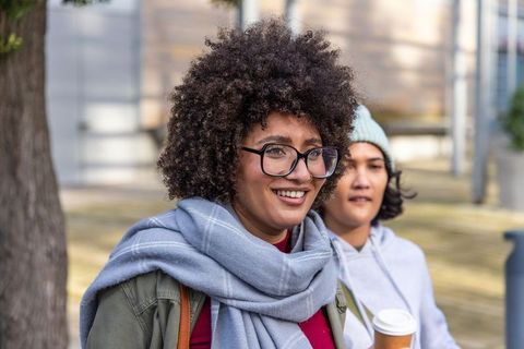 Smiling friends strolling downtown wearing cozy scarves and glasses while holding coffee