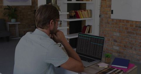 Male developer analyzing code on laptop in modern brick wall office