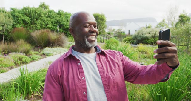 Image of happy senior american african men in the garden. Retirement lifestyle, spending time alone,technology.
