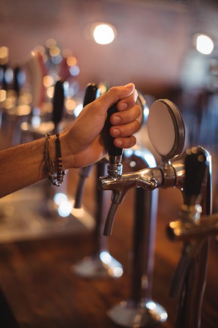Close-up of bartender's hand operating a beer tap in a pub. Ideal for use in articles or advertisements related to nightlife, bars, pubs, hospitality industry, and beverage services. Can also be used for illustrating concepts of social gatherings, bartending skills, and alcohol consumption.