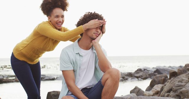 African american woman closing eyes of her husband from behind on the rocks near the sea. love and relationship concept