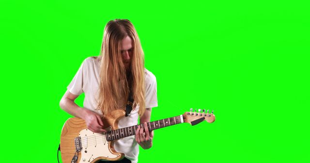 Image shows young musician playing electric guitar against a green screen. Ideal for use in promotional materials, concert posters, music industry advertising, educational content about guitar playing, or any creative project requiring a musician with a green screen background for added visual effects.