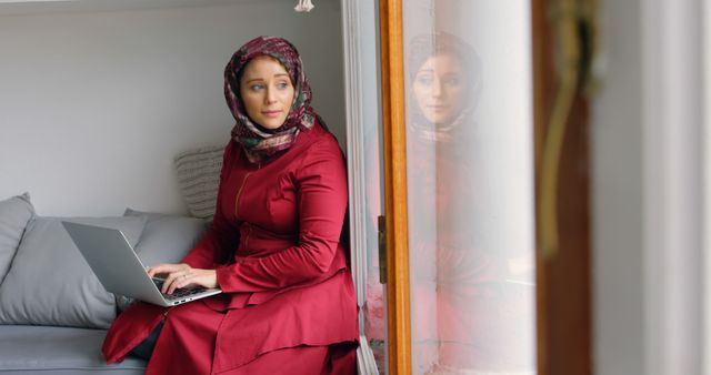 Woman Wearing Hijab Working on Laptop and Looking Out Window - Download Free Stock Images Pikwizard.com