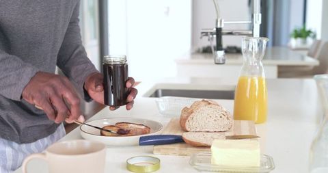 African american man spreading jam on toast in bright minimalist kitchen morning routine
