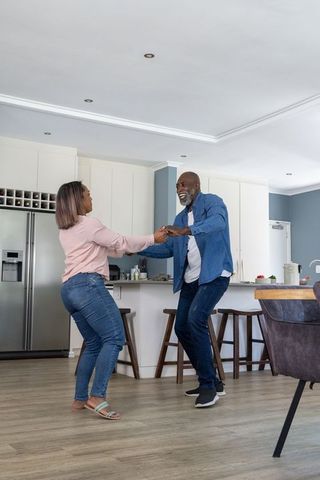 Mature couple dancing in modern kitchen, holding hands and laughing in open-plan home