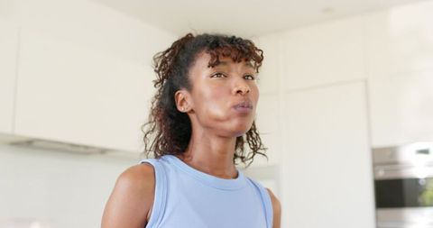 African american woman gazing thoughtfully in bright modern kitchen wearing blue top